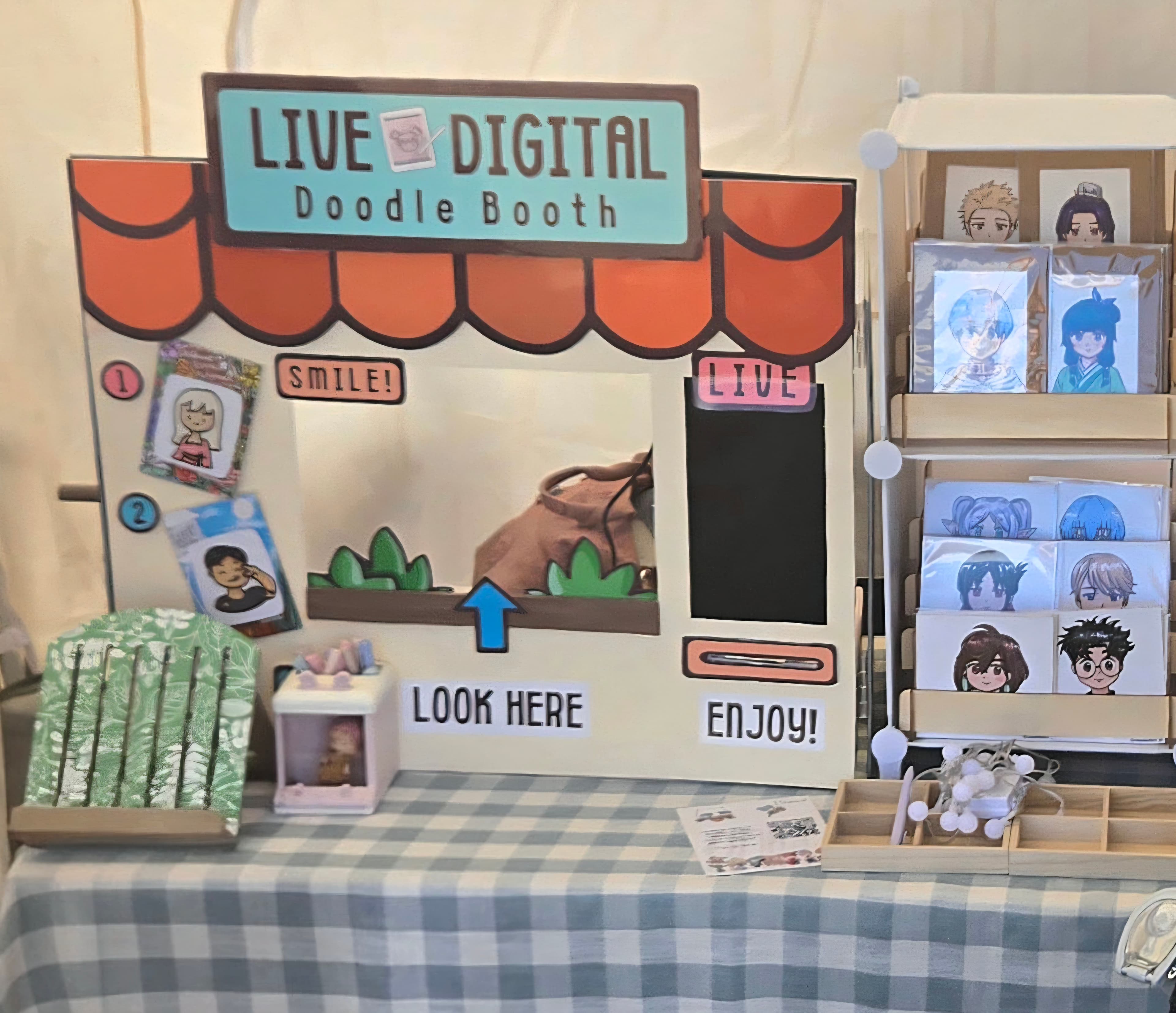 The Live Doodle Booth display at a market, with sample portraits and prints.
